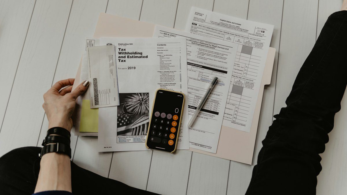Manos revisando documentos con un celular y una calculadora sobre la mesa