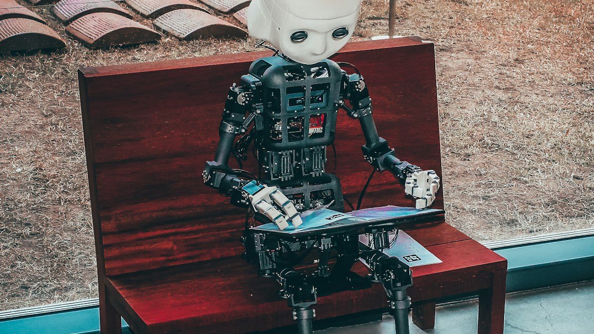 Pequeño robot humanoide sentado en un banco leyendo